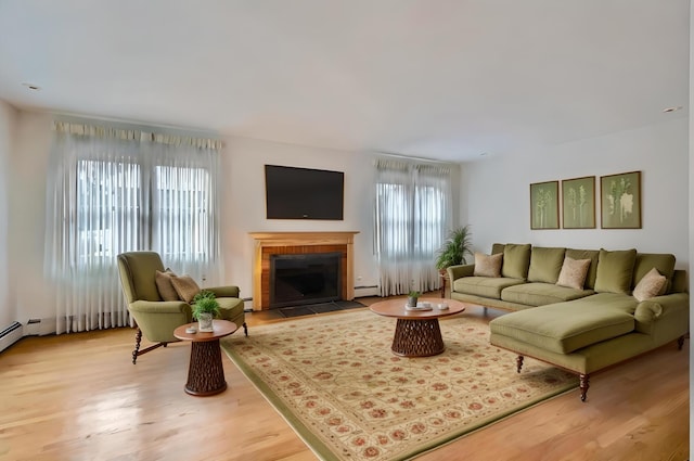 living room featuring baseboard heating, light hardwood / wood-style floors, and a brick fireplace