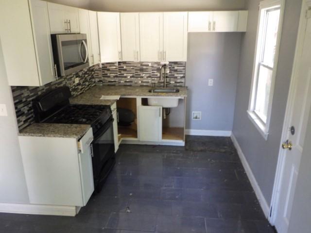 7732 S Muskegon Ave, Chicago, IL 60649 - kitchen with stainless steel microwave, black gas range, decorative backsplash, baseboards, and white cabinets
