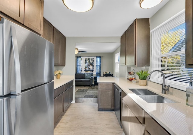 kitchen with kitchen peninsula, appliances with stainless steel finishes, ceiling fan, sink, and light hardwood / wood-style floors