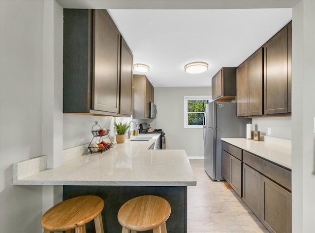 kitchen featuring dark brown cabinetry, sink, stainless steel appliances, kitchen peninsula, and a breakfast bar