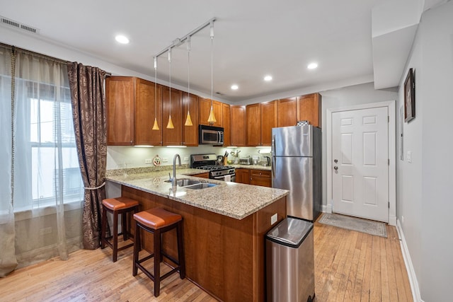 kitchen with stainless steel appliances, light stone countertops, sink, kitchen peninsula, and light hardwood / wood-style flooring