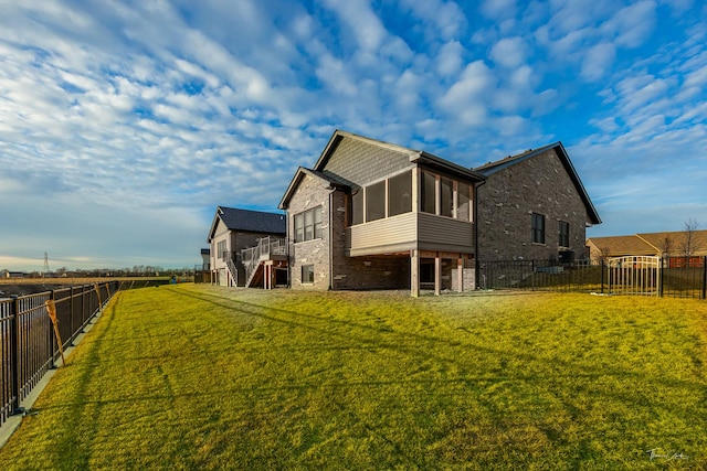 rear view of house featuring a fenced backyard, a yard, a sunroom, brick siding, and stairs