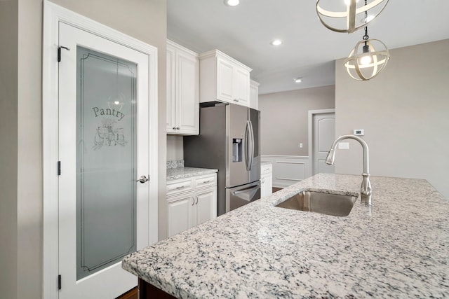 kitchen featuring stainless steel fridge, white cabinetry, light stone countertops, decorative light fixtures, and sink