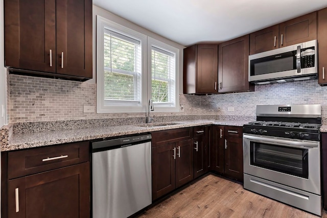 kitchen with decorative backsplash, light stone counters, appliances with stainless steel finishes, light wood-type flooring, and sink