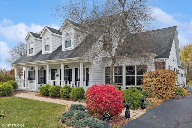 cape cod home featuring covered porch and a front lawn