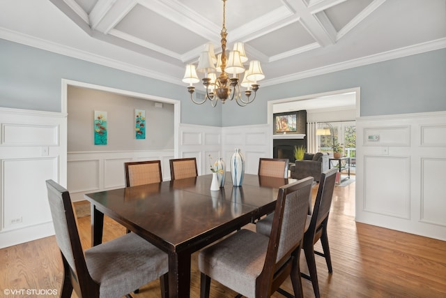 dining space featuring hardwood / wood-style floors, ornamental molding, coffered ceiling, and an inviting chandelier