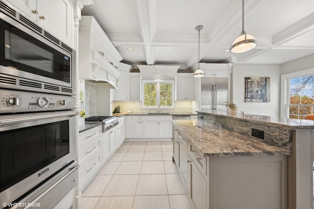 kitchen with built in appliances, sink, a center island, decorative light fixtures, and white cabinetry