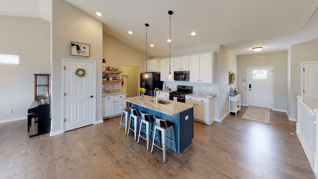 kitchen with white cabinetry, hanging light fixtures, black appliances, and a kitchen island with sink