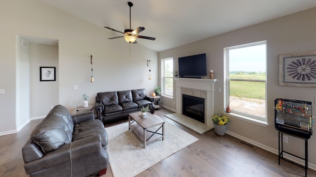 living room with a tiled fireplace, vaulted ceiling, light wood-type flooring, and ceiling fan