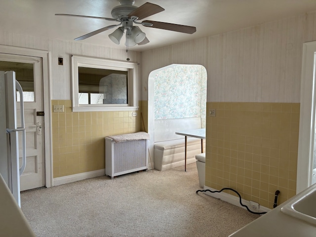 interior space with light carpet, radiator heating unit, tile walls, and ceiling fan