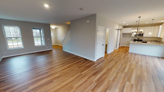 kitchen featuring light hardwood / wood-style flooring, hanging light fixtures, stainless steel appliances, light stone countertops, and white cabinets