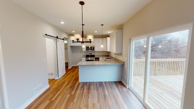 kitchen with hanging light fixtures, appliances with stainless steel finishes, white cabinetry, a barn door, and light wood-type flooring