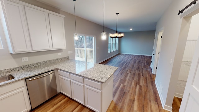 kitchen with kitchen peninsula, white cabinetry, a barn door, stainless steel dishwasher, and light hardwood / wood-style flooring