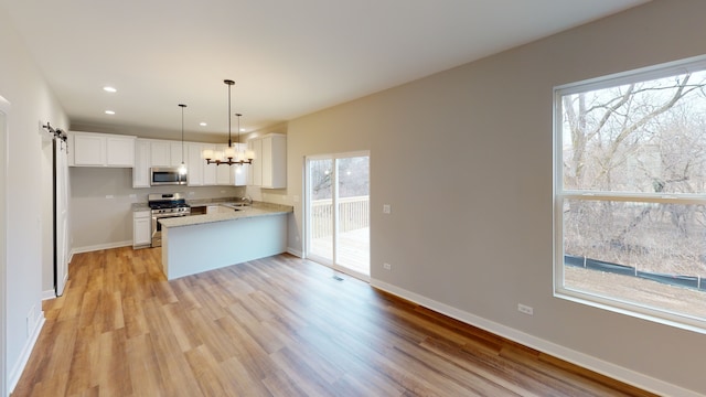 kitchen with stainless steel appliances, a wealth of natural light, kitchen peninsula, and white cabinets