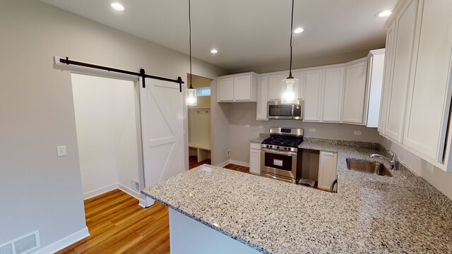 kitchen with light hardwood / wood-style flooring, stainless steel appliances, sink, decorative light fixtures, and white cabinets