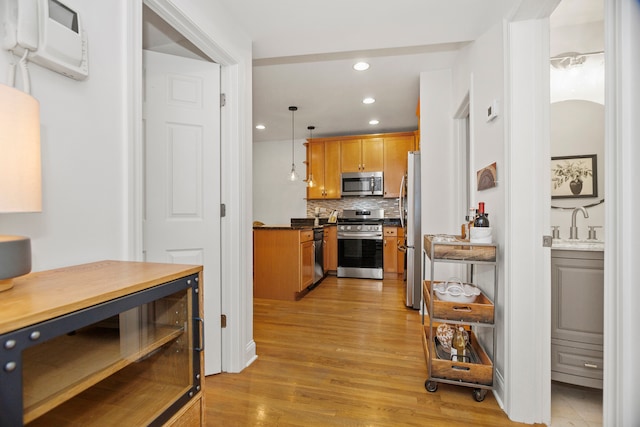 kitchen with appliances with stainless steel finishes, tasteful backsplash, an AC wall unit, decorative light fixtures, and light wood-type flooring