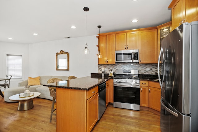 kitchen featuring appliances with stainless steel finishes, decorative light fixtures, hardwood / wood-style flooring, a breakfast bar, and kitchen peninsula