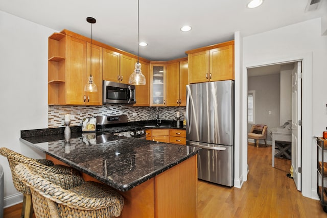 kitchen with stainless steel appliances, light hardwood / wood-style floors, kitchen peninsula, dark stone countertops, and decorative light fixtures