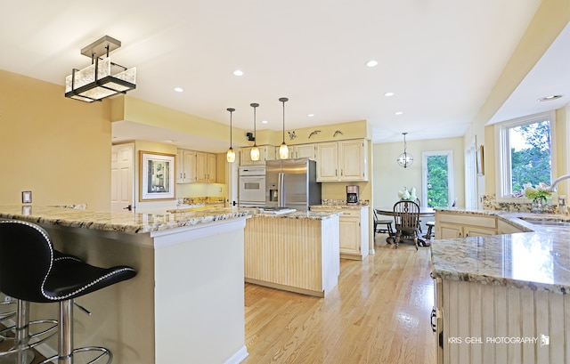 kitchen with light hardwood / wood-style floors, hanging light fixtures, a kitchen island, and stainless steel fridge