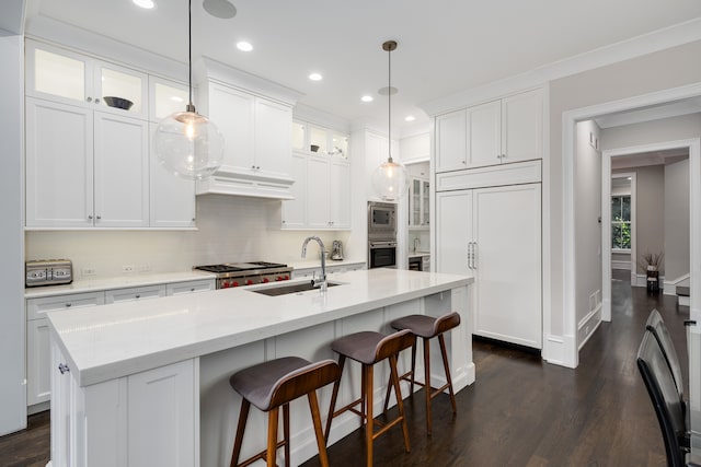 kitchen with sink, built in appliances, a kitchen island with sink, and white cabinetry