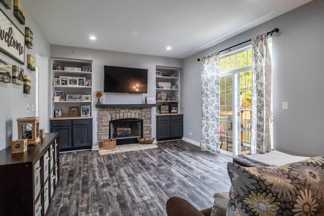 living room with a stone fireplace, built in features, and dark hardwood / wood-style flooring