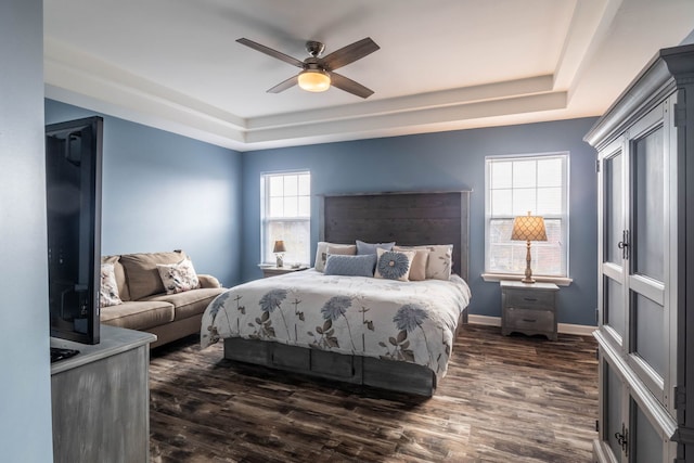 bedroom with dark wood-type flooring, ceiling fan, and a tray ceiling