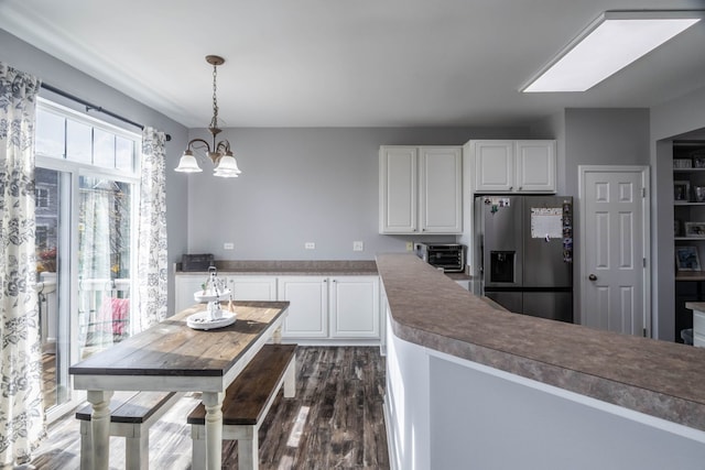 kitchen with stainless steel fridge, dark hardwood / wood-style flooring, white cabinetry, a skylight, and pendant lighting