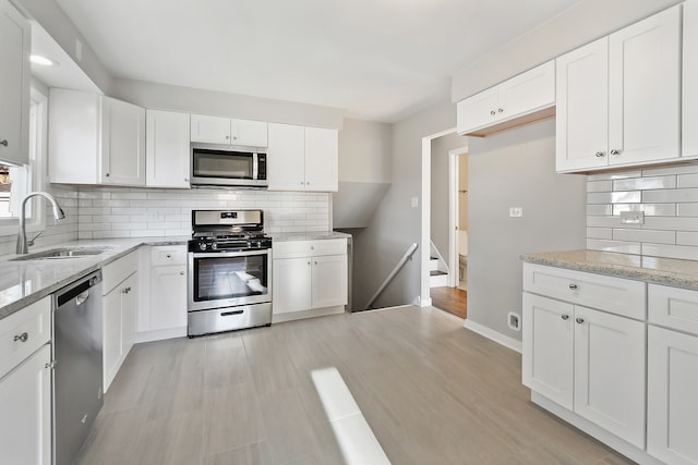 kitchen with white cabinetry, light stone countertops, stainless steel appliances, and sink