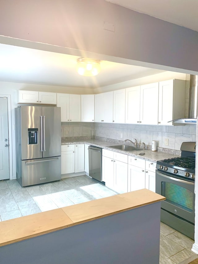 kitchen featuring wall chimney exhaust hood, stainless steel appliances, sink, white cabinets, and tasteful backsplash