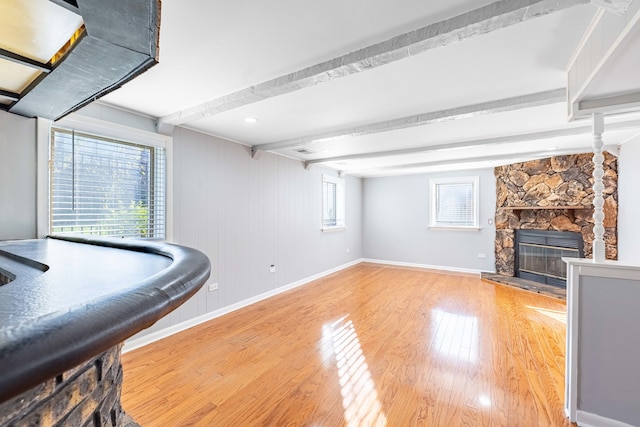 interior space with a stone fireplace, hardwood / wood-style floors, and beam ceiling