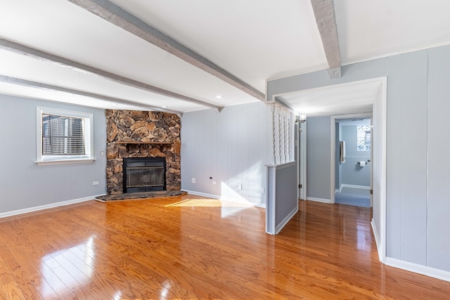 unfurnished living room with wood-type flooring, a healthy amount of sunlight, a stone fireplace, and beam ceiling