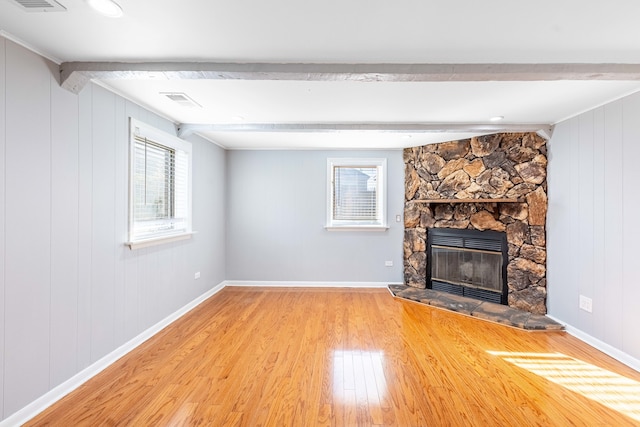 unfurnished living room with ornamental molding, a stone fireplace, beam ceiling, wood walls, and hardwood / wood-style floors