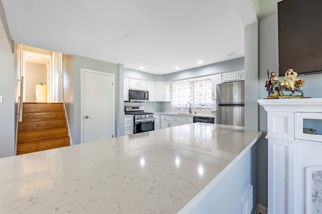 kitchen featuring white cabinetry, sink, appliances with stainless steel finishes, light stone countertops, and backsplash