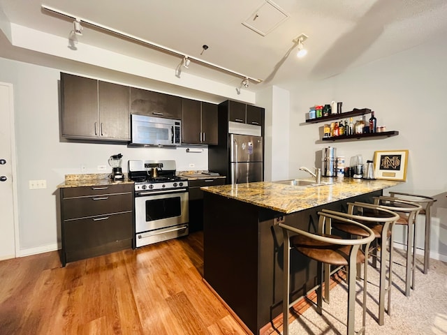 kitchen featuring light wood-type flooring, kitchen peninsula, rail lighting, stainless steel appliances, and a breakfast bar