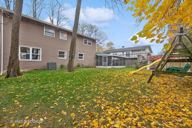 back of property featuring a playground, central air condition unit, a sunroom, and a lawn