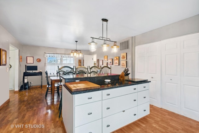 kitchen with decorative light fixtures, hardwood / wood-style flooring, white cabinets, a center island, and a breakfast bar area