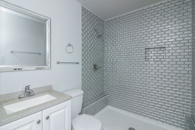 bathroom with vanity, tiled shower, and toilet