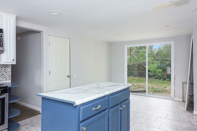 kitchen with a kitchen island, light hardwood / wood-style flooring, backsplash, blue cabinets, and light stone counters