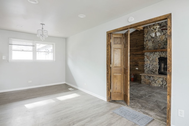 empty room featuring hardwood / wood-style floors, a stone fireplace, and a chandelier