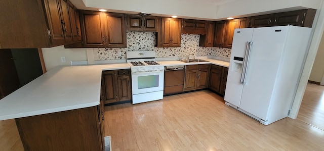 kitchen with sink, kitchen peninsula, white appliances, light wood-type flooring, and decorative backsplash