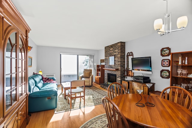 dining space with a brick fireplace, light hardwood / wood-style floors, and a chandelier