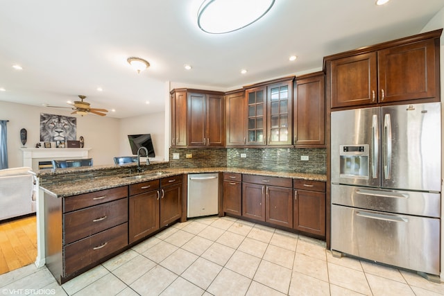 kitchen with appliances with stainless steel finishes, sink, kitchen peninsula, dark stone countertops, and light tile patterned floors