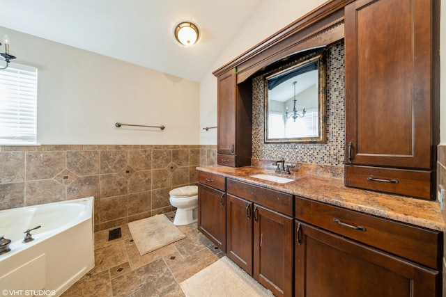 bathroom with toilet, tile walls, vaulted ceiling, a bathing tub, and vanity