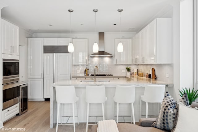 kitchen featuring white cabinetry, wall chimney range hood, decorative light fixtures, and backsplash