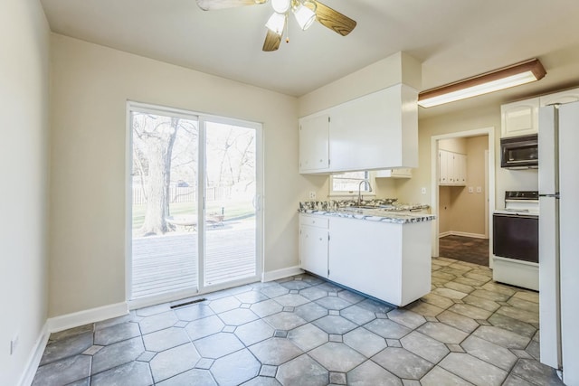 kitchen with white appliances, sink, ceiling fan, light stone counters, and white cabinetry