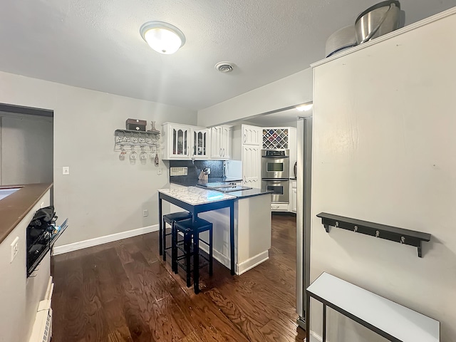 kitchen featuring a kitchen breakfast bar, white cabinetry, dark wood-type flooring, and double oven