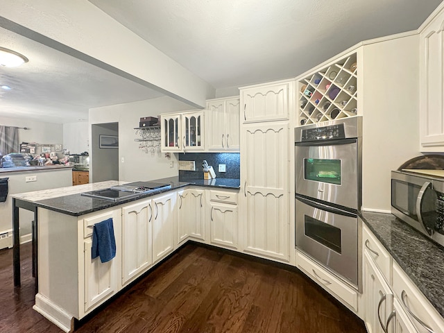 kitchen featuring kitchen peninsula, a kitchen breakfast bar, dark stone counters, stainless steel appliances, and dark hardwood / wood-style floors