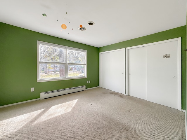 unfurnished bedroom with light carpet, two closets, and a baseboard radiator