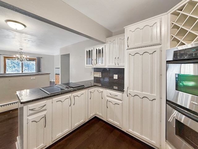 kitchen featuring dark wood-type flooring, kitchen peninsula, appliances with stainless steel finishes, a notable chandelier, and white cabinetry