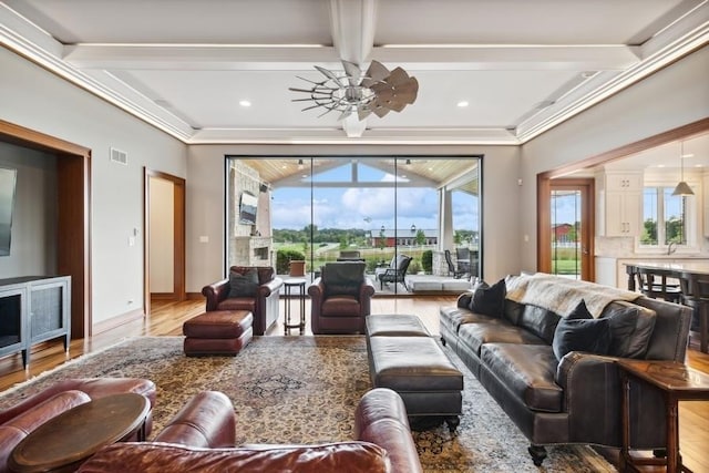 living room with light wood-type flooring, ornamental molding, coffered ceiling, ceiling fan, and beamed ceiling